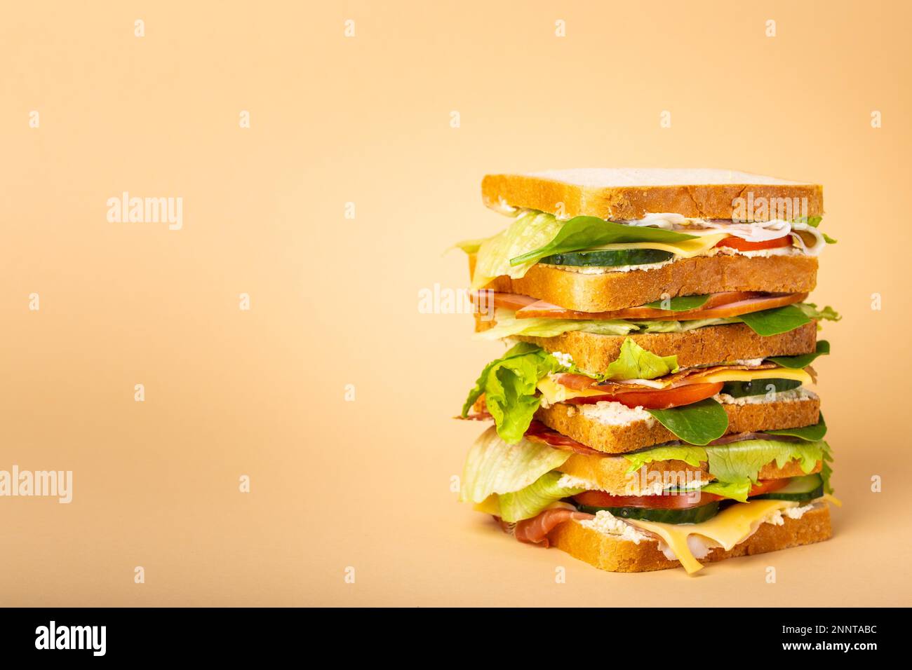 Nahaufnahme eines großen, leckeren Sandwichs mit Käse, Schinken, Prosciutto, frischem Salat, Tomaten, Gurken auf pastellgelbem Hintergrund. Gesunder Feinschmecker Stockfoto