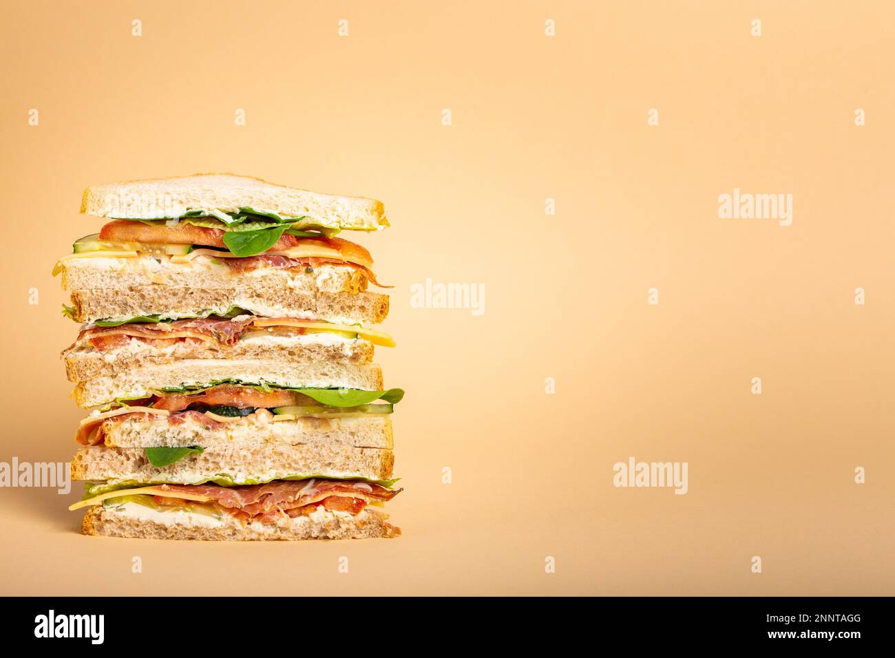 Nahaufnahme eines großen, leckeren Sandwichs mit Käse, Schinken, Prosciutto, frischem Salat, Tomaten, Gurken auf pastellgelbem Hintergrund. Gesunder Feinschmecker Stockfoto