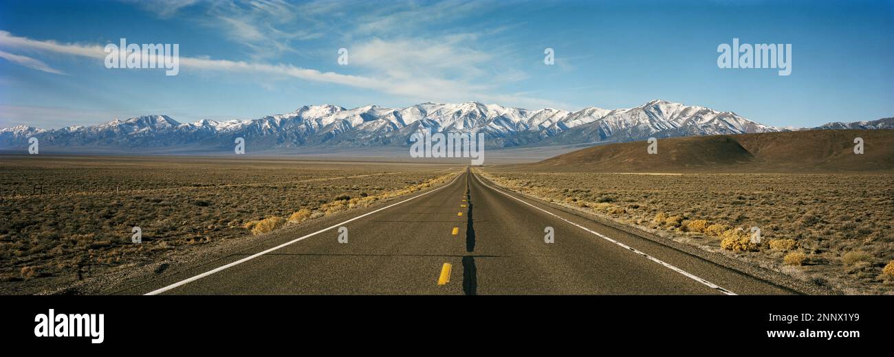 Gerade Straße in der Wüste und die Rocky Mountains im Hintergrund, Colorado, USA Stockfoto