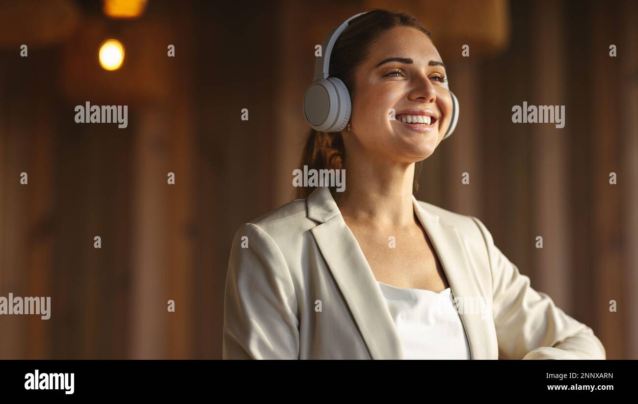 Glückliche Geschäftsfrau mit kabellosen Kopfhörern im Büro. Professionelle Geschäftsfrau, die bei der Arbeit eine Musik-Playlist hört. Stockfoto