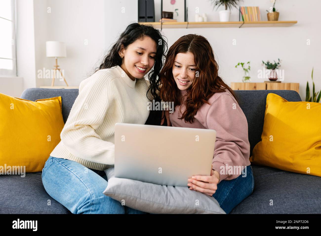 Glückliche studentin aus lateinamerika, die zu Hause auf dem Sofa mit einem Laptop sitzt Stockfoto