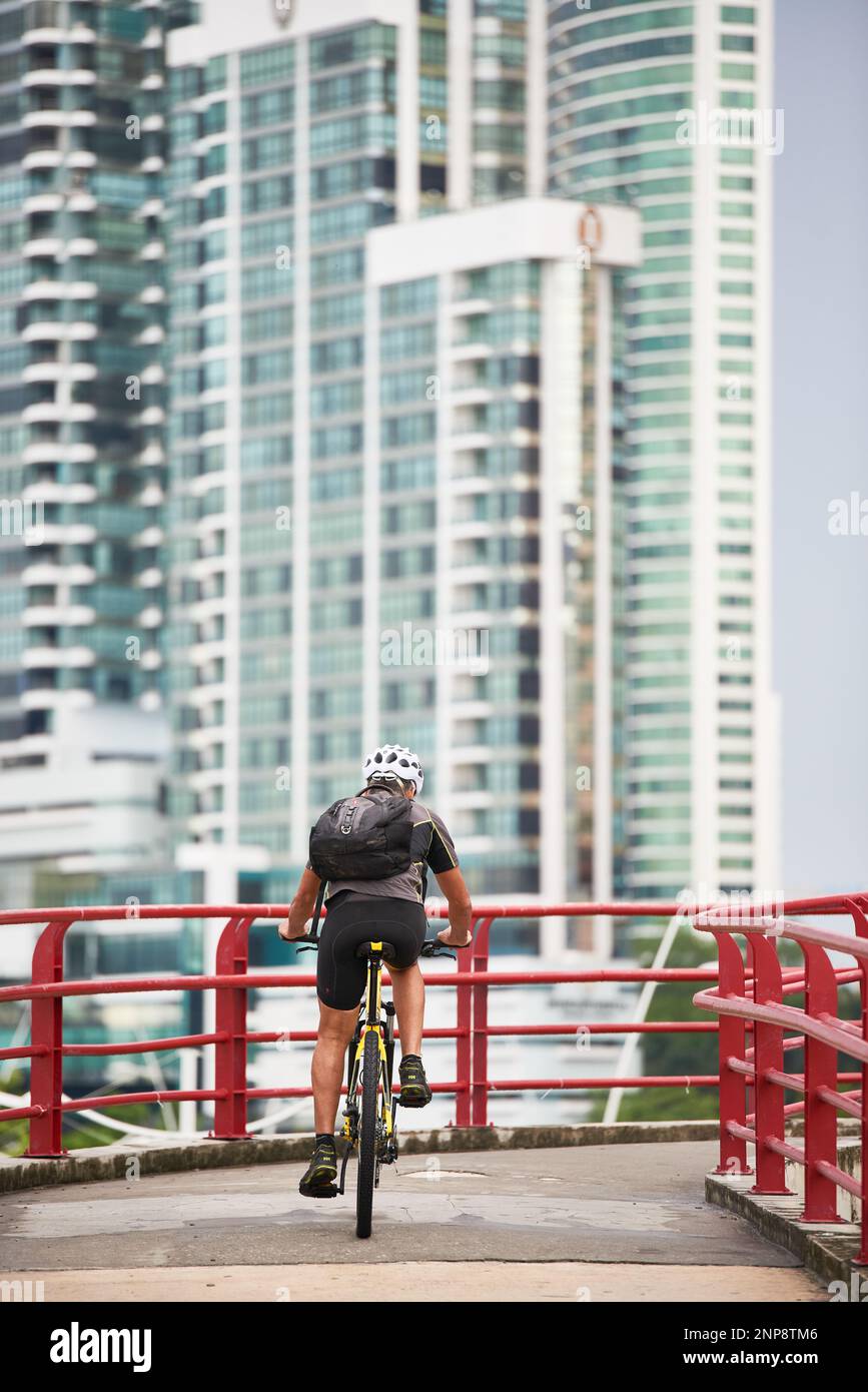 Radfahrer von hinten gesehen, mit weißem Helm und Rucksack auf dem Rücken, der durch die Stadt Panama, Panama-Stadt, Panama, Republik Panam zirkuliert Stockfoto