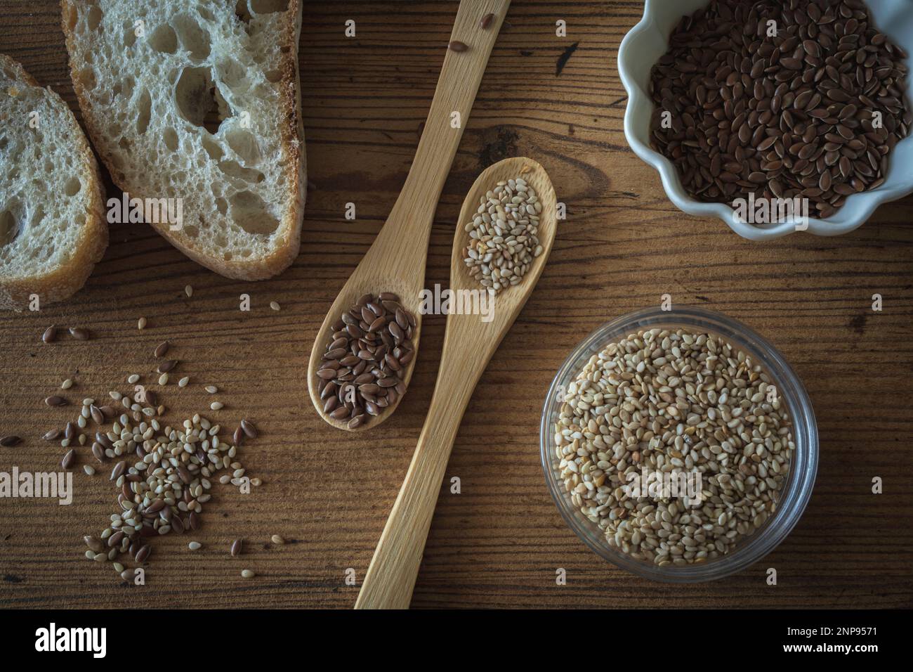 Gesundes Stillleben mit Sesam- und Leinsamen in Schüsseln und Holzlöffeln und in einer Ecke natürlichem Brot Stockfoto