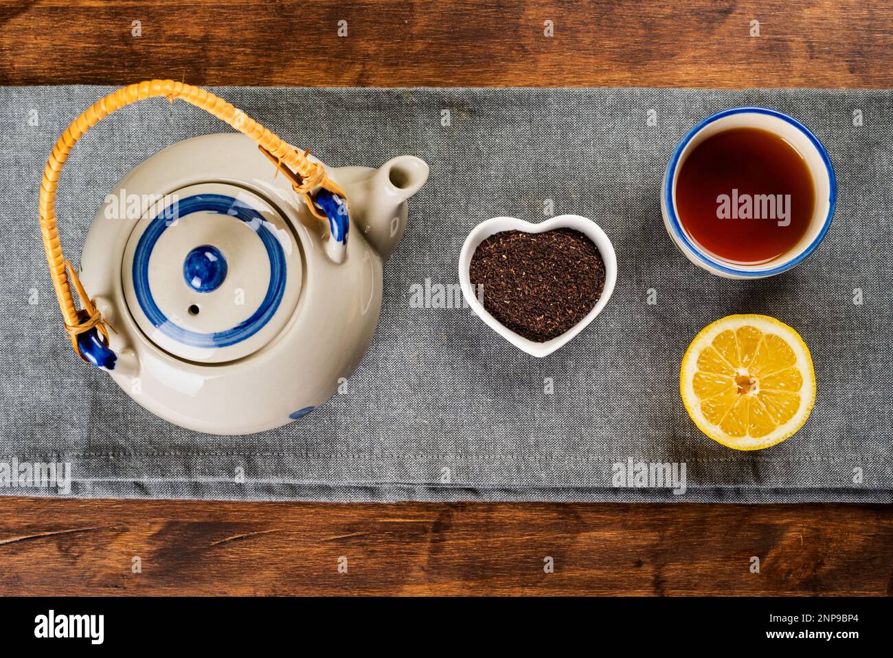 Porzellan-Teekanne neben einer kleinen herzförmigen Schüssel mit gemahlenem Tee, einer Tasse mit Tee und einer halben Zitrone. Stockfoto
