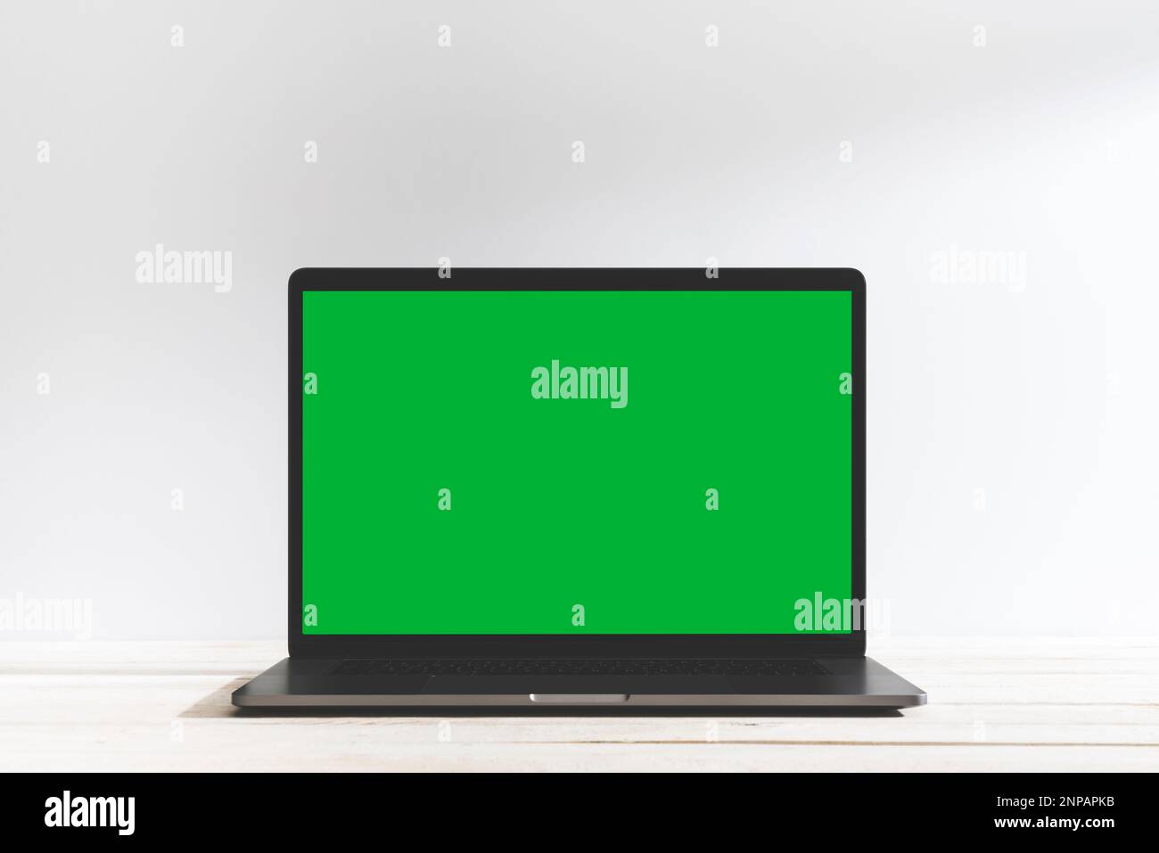 Chroma Key Laptop mit grünem Bildschirm auf dem Tisch vor dem weißen Hintergrund. Tischaufnahme des Innenraums mit Fensterlichteffekt. Stockfoto