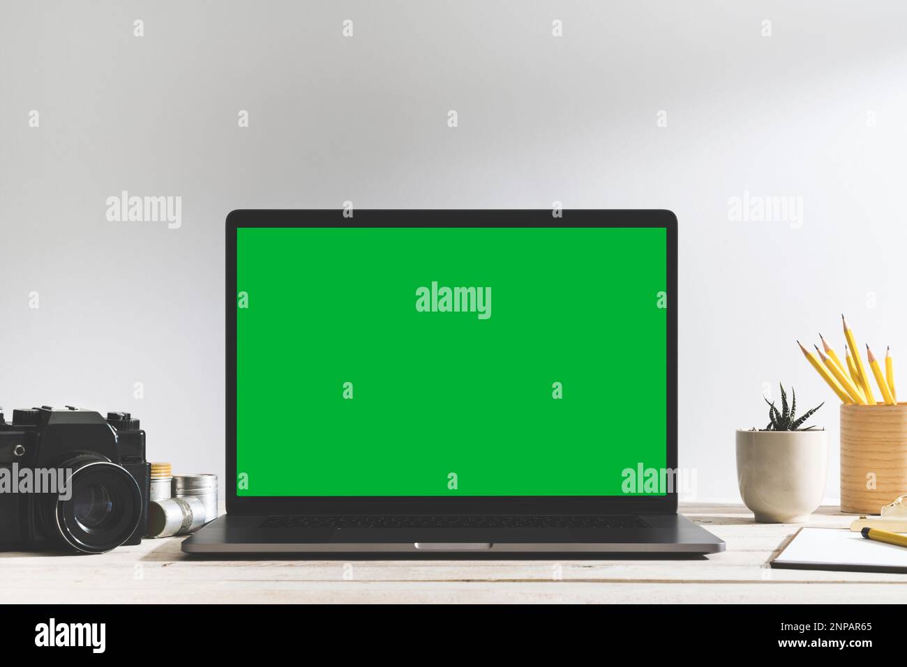 Chroma Key Laptop mit grünem Bildschirm und Fotoausrüstung auf dem Tisch vor dem weißen Hintergrund. Tischaufnahme des Innenraums mit effektivem Fensterlicht Stockfoto