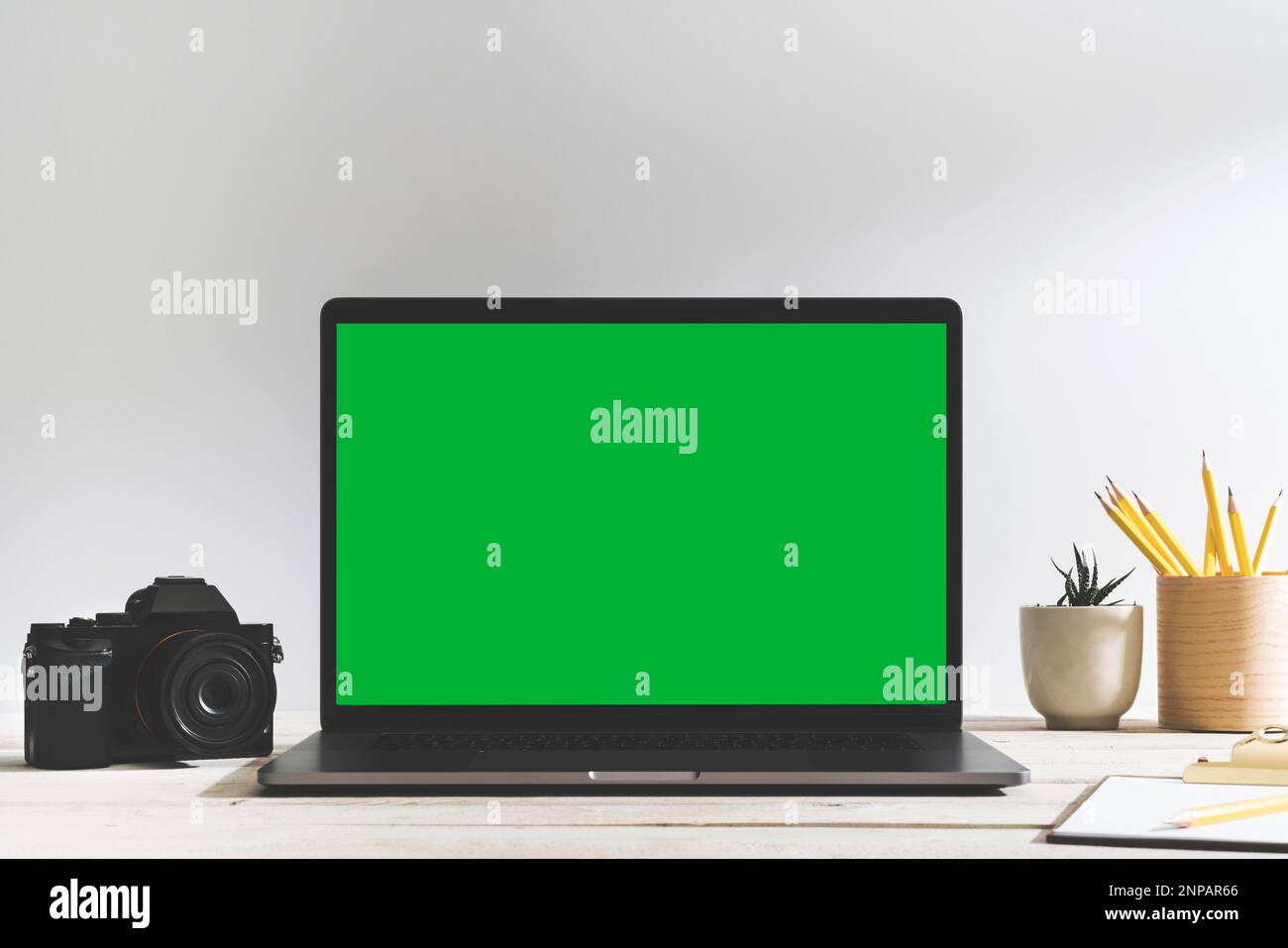 Laptop mit grünem Bildschirm und Digitalkamera mit Chroma Key auf dem Tisch vor dem weißen Hintergrund. Tischaufnahme des Innenraums mit Fensterlichteffekt. Stockfoto