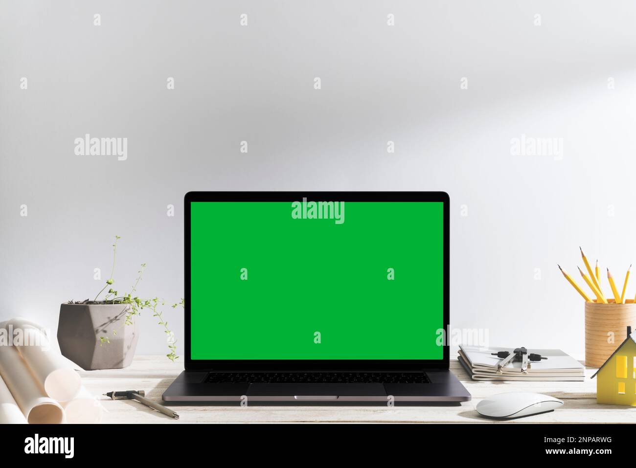Chroma Key Laptop mit grünem Bildschirm auf dem Tisch des Designers vor dem weißen Hintergrund. Tischaufnahme des Innenraums mit Fensterlichteffekt. Stockfoto