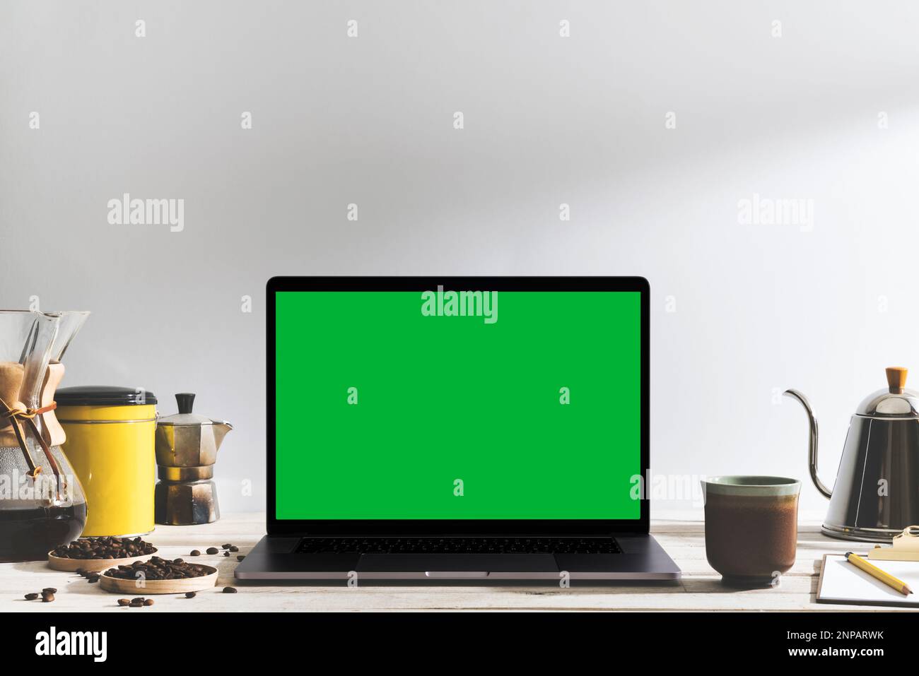 Laptop mit grünem Chroma Key-Bildschirm und Werkzeuge zum Brühen von Kaffee auf dem Tisch vor dem weißen Hintergrund. Tischaufnahme des Innenraums mit effektivem Fensterlicht Stockfoto