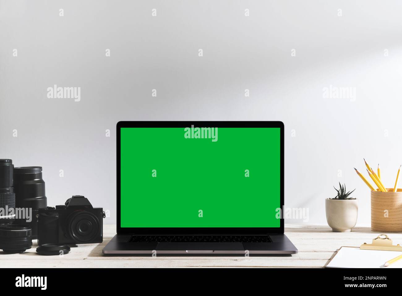 Chroma Key Laptop mit grünem Bildschirm und Fotoausrüstung auf dem Tisch vor dem weißen Hintergrund. Tischaufnahme des Innenraums mit Fensterbeleuchtung eff Stockfoto