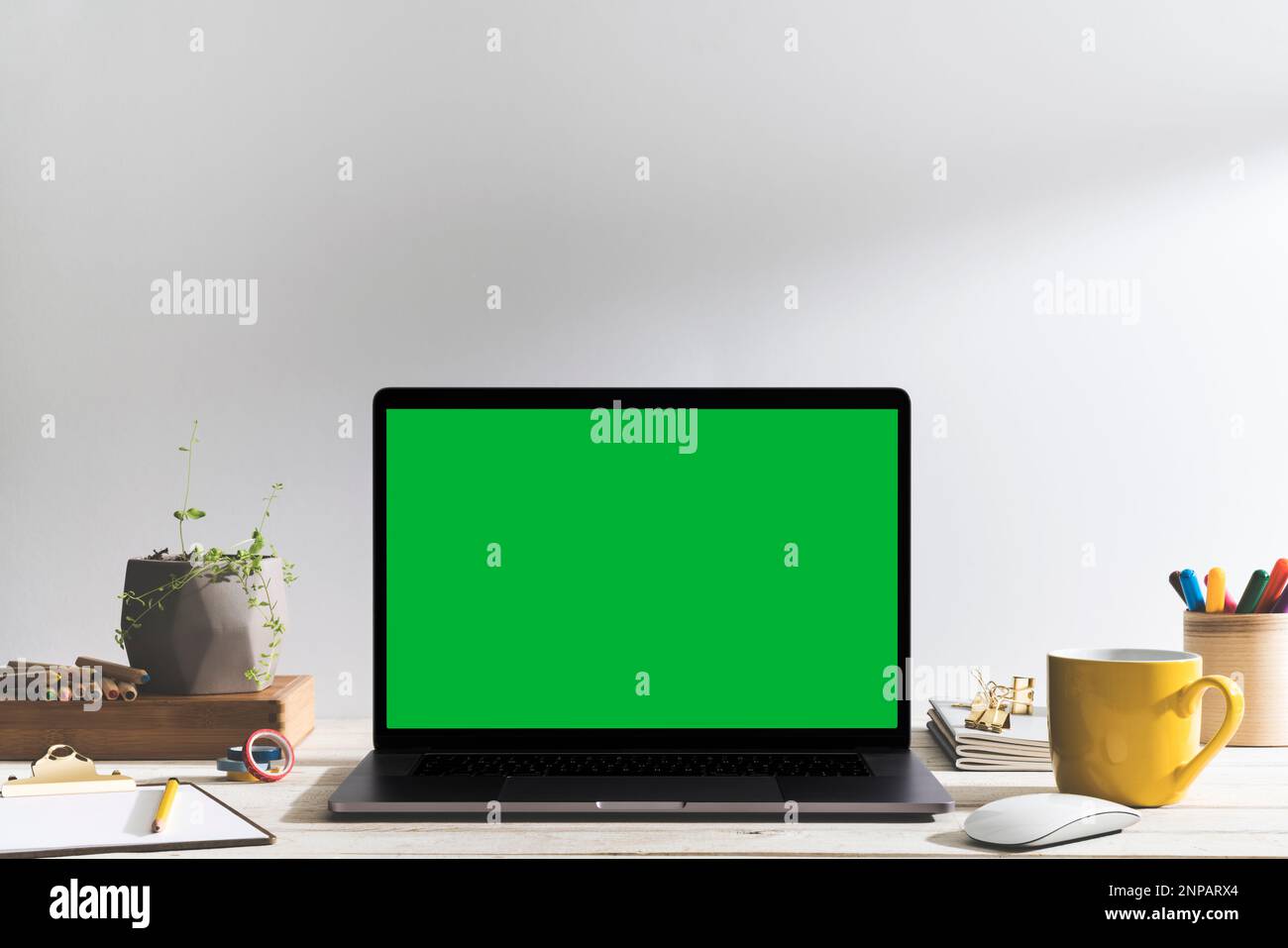 Chroma Key Laptop mit grünem Bildschirm auf dem Tisch des Illustrators vor dem weißen Hintergrund. Tischaufnahme des Innenraums mit Fensterlichteffekt. Stockfoto