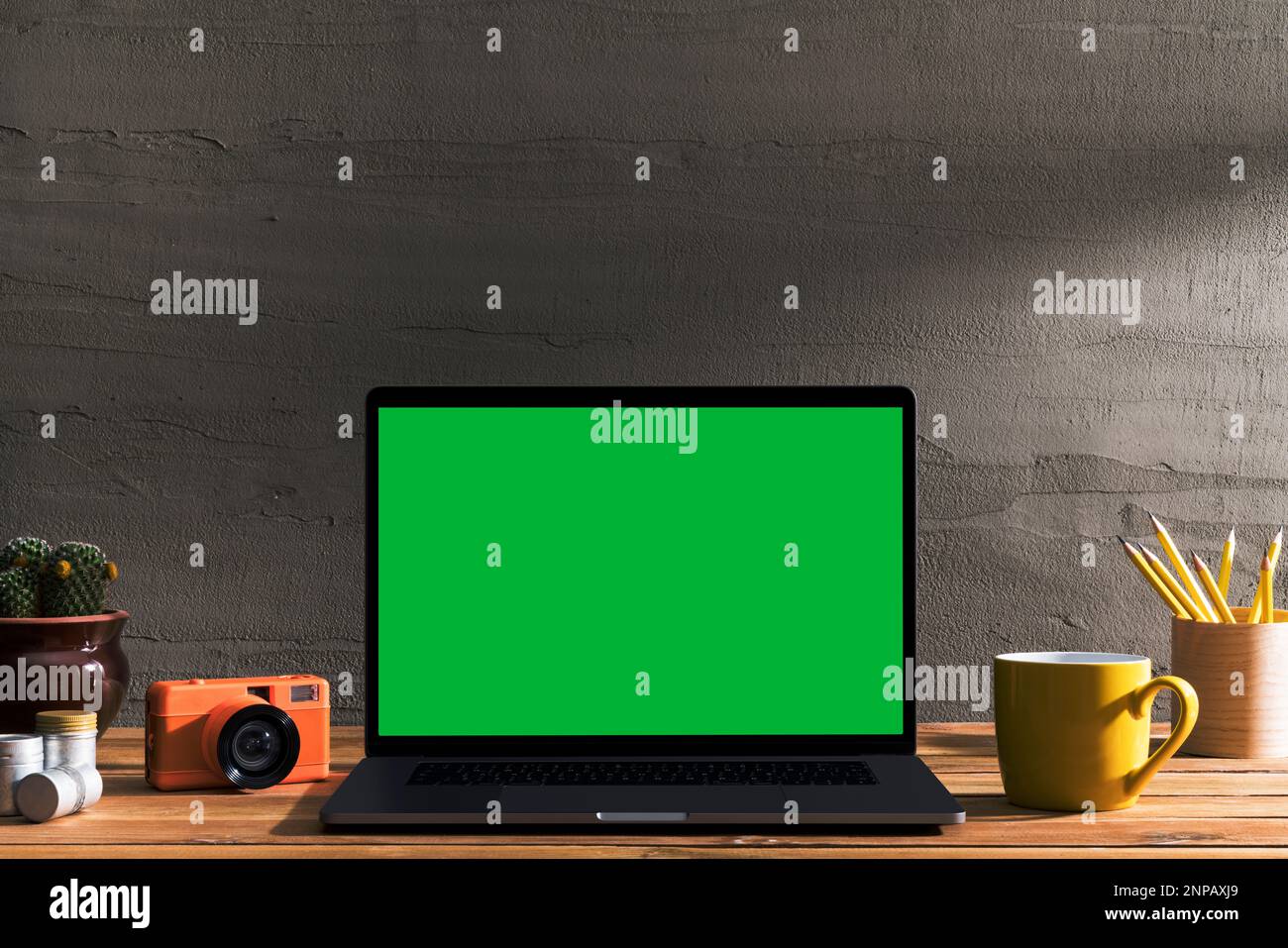Chroma Key Laptop mit grünem Bildschirm und Fotoausrüstung auf Holztisch vor Betonwand. Tischaufnahme des Innenraums mit Fensterbeleuchtung Stockfoto