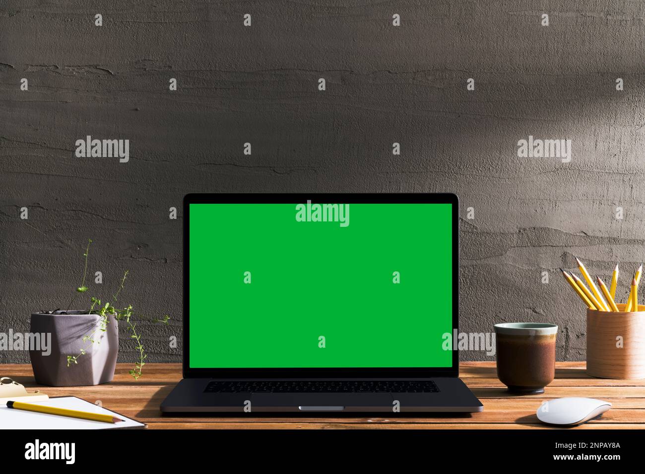 Chroma Key Laptop mit grünem Bildschirm auf Holztisch vor Betonwand. Tischaufnahme des Innenraums mit Fensterlichteffekt. Stockfoto