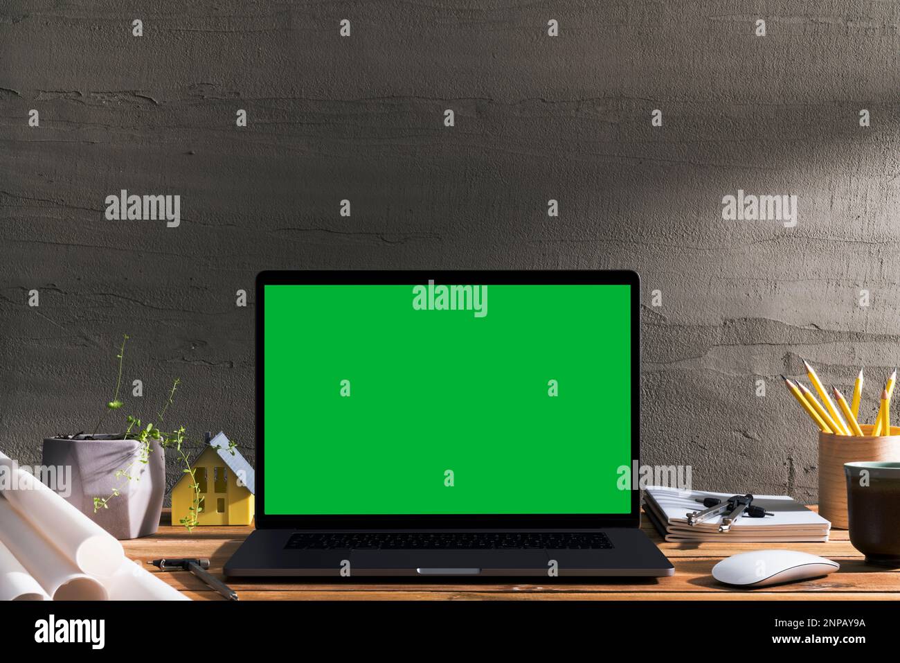 Chroma Key Laptop mit grünem Bildschirm auf Holztisch des Designers vor Betonwand. Tischaufnahme des Innenraums mit Fensterlichteffekt. Stockfoto