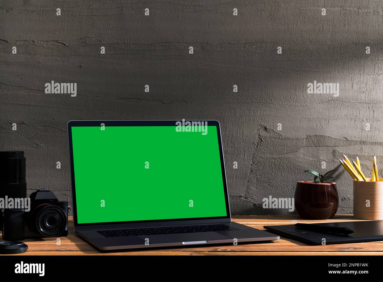 Chroma Key Green Screen, Laptop mit abgewinkelter Ansicht und digitaler Fotoausrüstung auf Holztisch vor Betonwand. Tischaufnahme der Innenräume Stockfoto