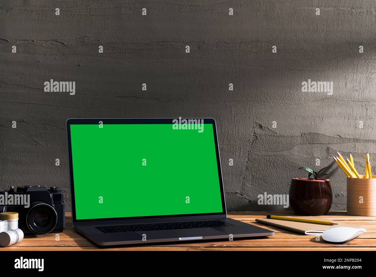 Chroma Key Green Screen, abgewinkelter Laptop mit Fotoausrüstung auf Holztisch vor Betonwand. Tischaufnahme des Innenraums mit Stockfoto