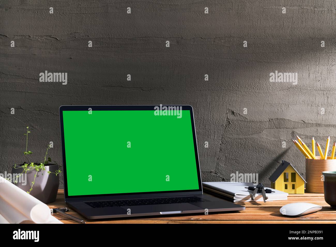 Chroma Key Green Screen, Laptop mit abgewinkelter Sicht auf Holztisch vor Betonwand. Tischaufnahme des Innenraums mit Fensterlichteffekt. Stockfoto