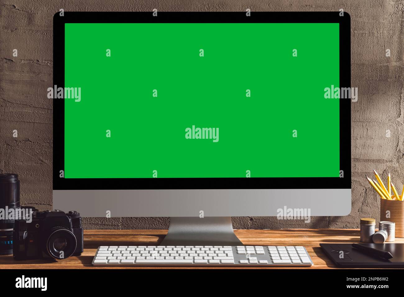 Chroma Key Green Screen Computer mit Fotoausrüstung auf dem Tisch. Tischaufnahme des Innenraums mit Fensterlichteffekt. Stockfoto
