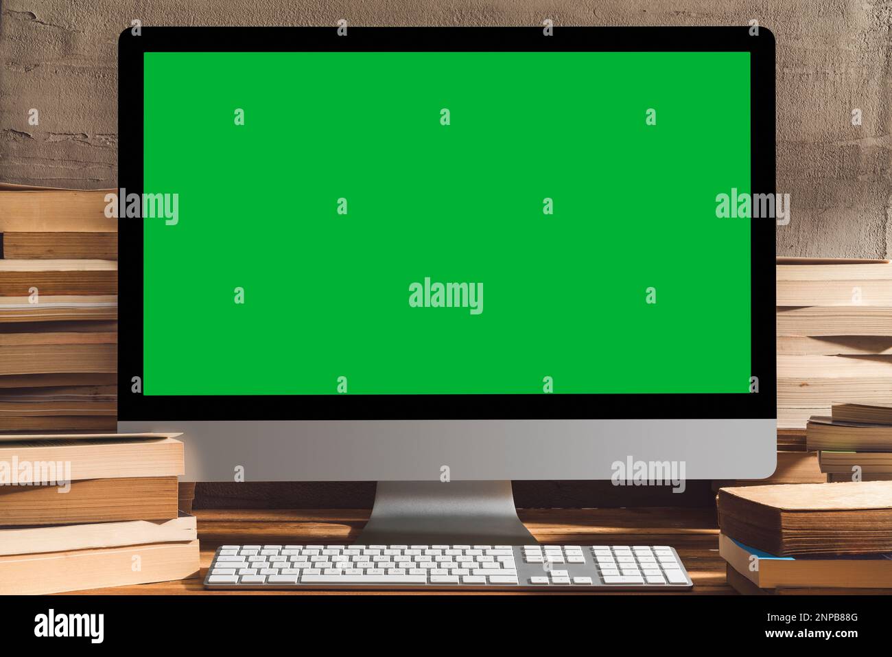 Chroma Key Computer mit grünem Bildschirm, Desktop-pc mit einem Stapel Bücher auf dem Tisch. Tischaufnahme des Innenraums mit Fensterlichteffekt. Stockfoto