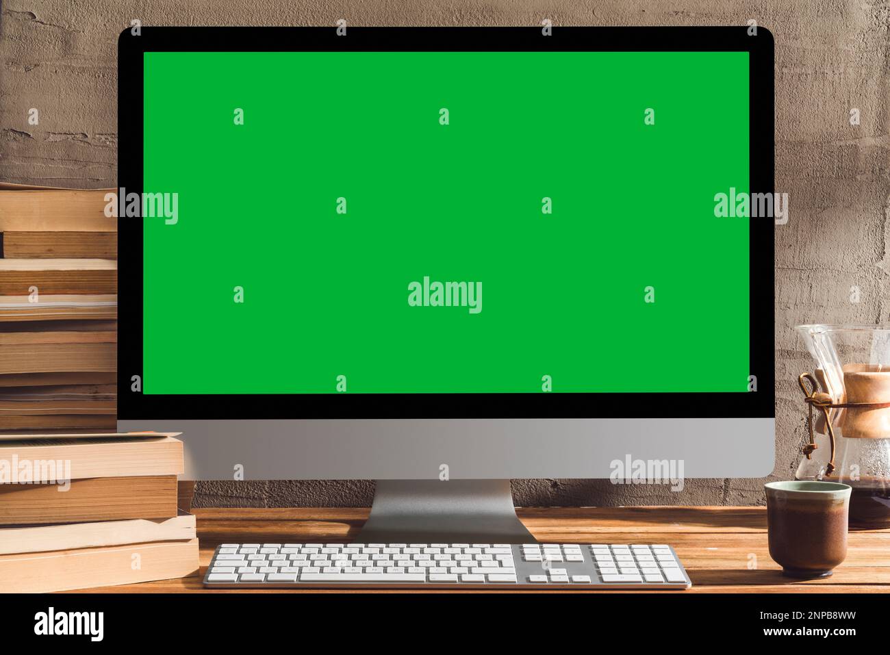 Chroma Key Computer mit grünem Bildschirm, Desktop-pc auf Tisch mit Bücherstapel und einer Tasse Kaffee. Tischaufnahme des Innenraums mit Fensterlichteffekt. Stockfoto