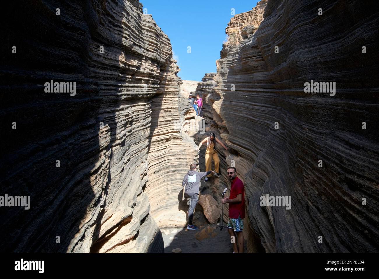 Touristen, die in Schichten von Ladera del volcan Las Grietas Lanzarote, Kanarische Inseln, Spanische vulkanische Felsformationen durch Erosion spazieren gehen Stockfoto
