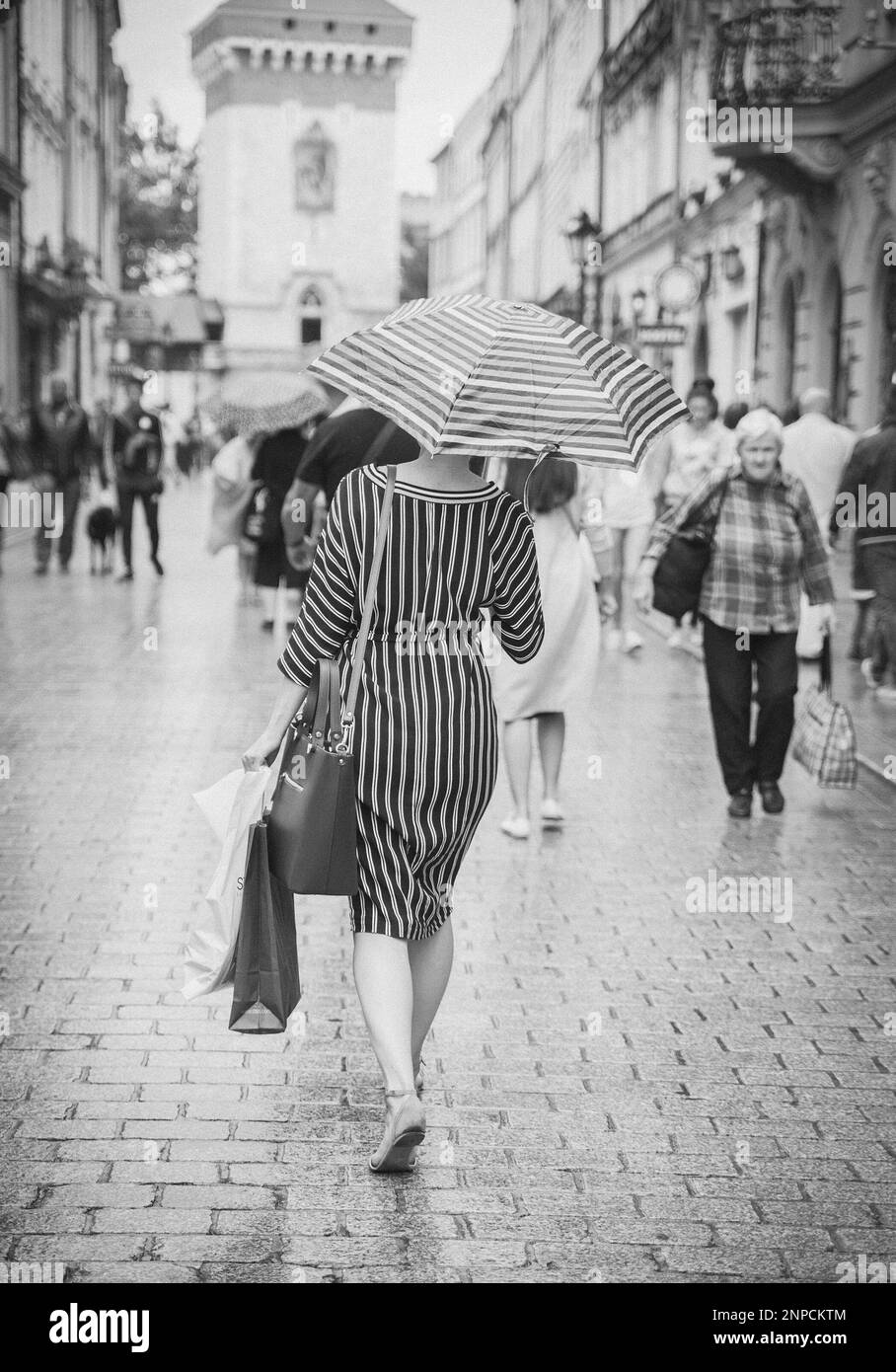 Eine schlanke Frau in einem gestreiften Kleid läuft mit gestreiftem Regenschirm in Warschau Stockfoto