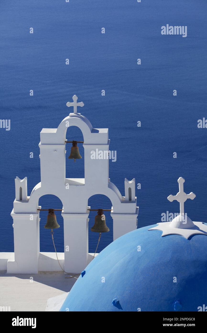 Ein Blick auf eine traditionelle Kirche mit blauer Kuppel und weißen Glockenturm mit dem Meer und der Caldera dahinter. Stockfoto