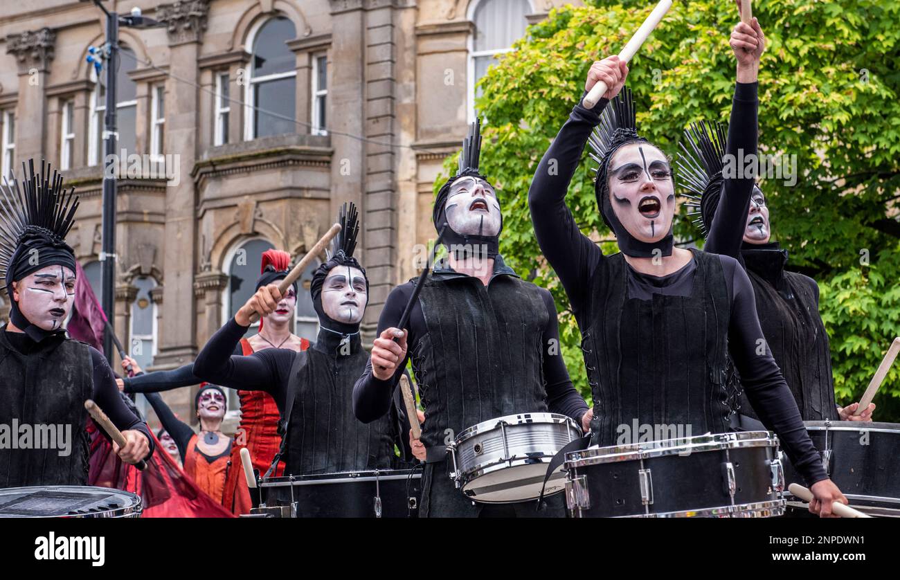 Eine Gruppe von Künstlern mit bemalten Gesichtern in schwarzen Anzügen und schwarzem Kopftuch mit Wappen schlagen auf ihre Trommeln, während sie auf dem Harrogate Carnival parieren. Stockfoto