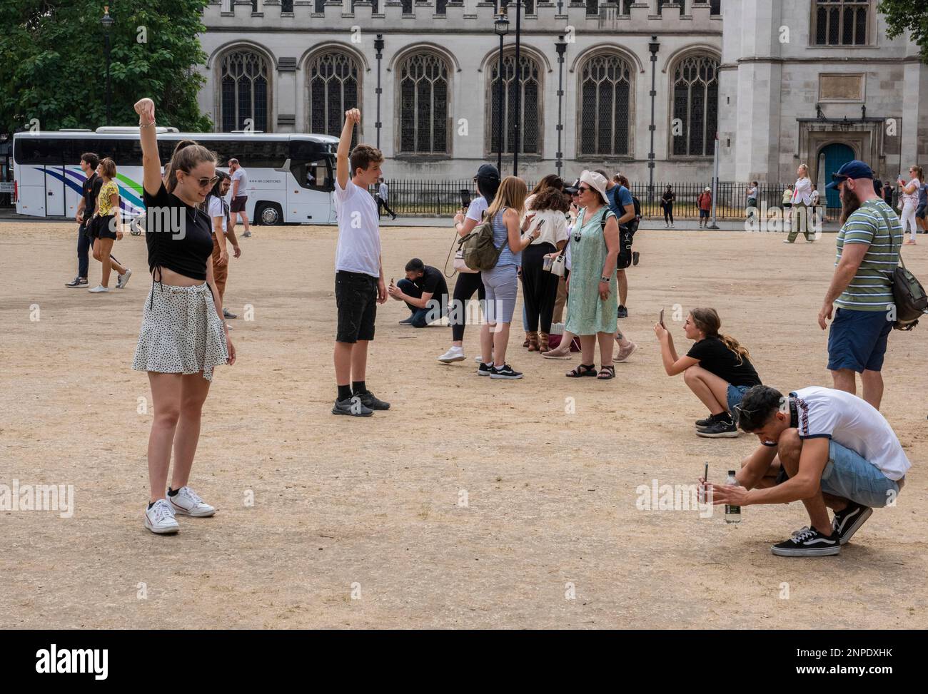 Touristen, die für Fotos posieren und so tun, als würden sie den Gipfel von Big Ben kneifen, stehen auf braunem, verbranntem Gras aufgrund der Sommerhitzewelle. Stockfoto