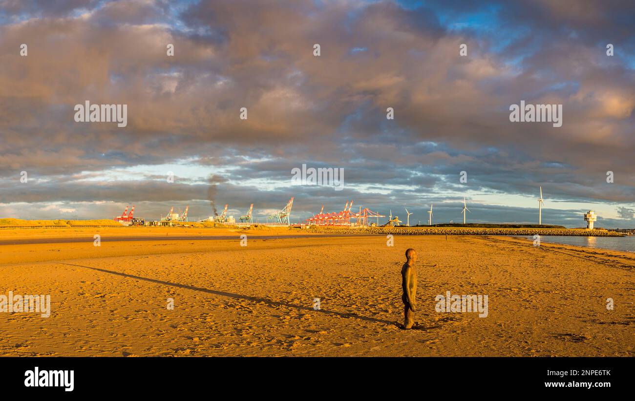 Die untergehende Sonne über der Irischen See schafft einen langen Schatten hinter einem der Iron Men an einem anderen Ort am Crosby Beach. Stockfoto