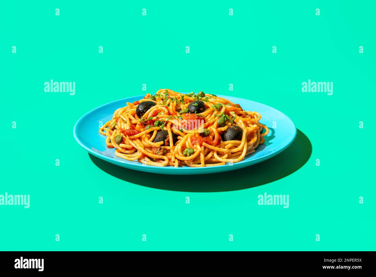 Teller mit Spaghetti puttanesca minimalist auf einem grünen Tisch. Vegane Pasta mit Kapern, schwarzen Oliven und Kirschtomaten. Stockfoto