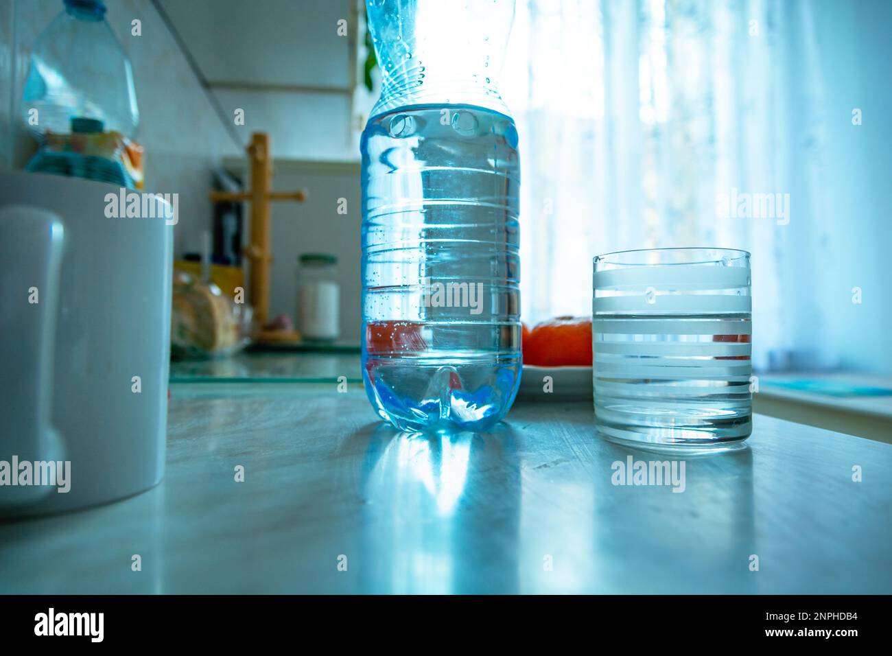 Eine Plastikflasche mit Wasser und ein leeres Glas stehen auf dem Küchentisch Stockfoto