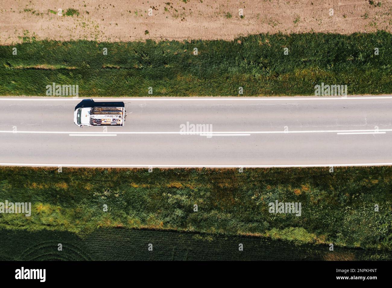 Drohnen-POV-Luftaufnahme eines kleinen LKWs, der am sonnigen Sommernachmittag auf der Autobahn durch nicht-städtische Landschaften fährt, direkt darüber Stockfoto