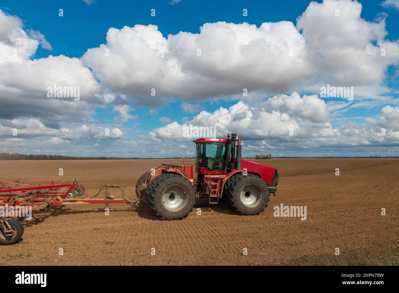 Roter Traktor pflügt an einem sonnigen Frühlingstag frischen Boden. Saisonarbeit auf dem Feld. Lebendige Landschaft Stockfoto