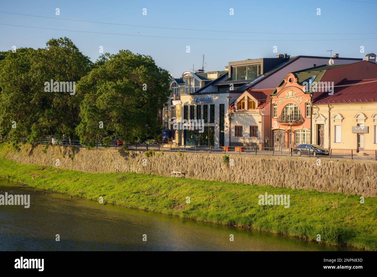 Stadtbild mit Fluss uzh. Ufer der Innenstadt mit alten Gebäuden am anderen Ufer in der Ferne. Sonniger Sommermorgen Stockfoto