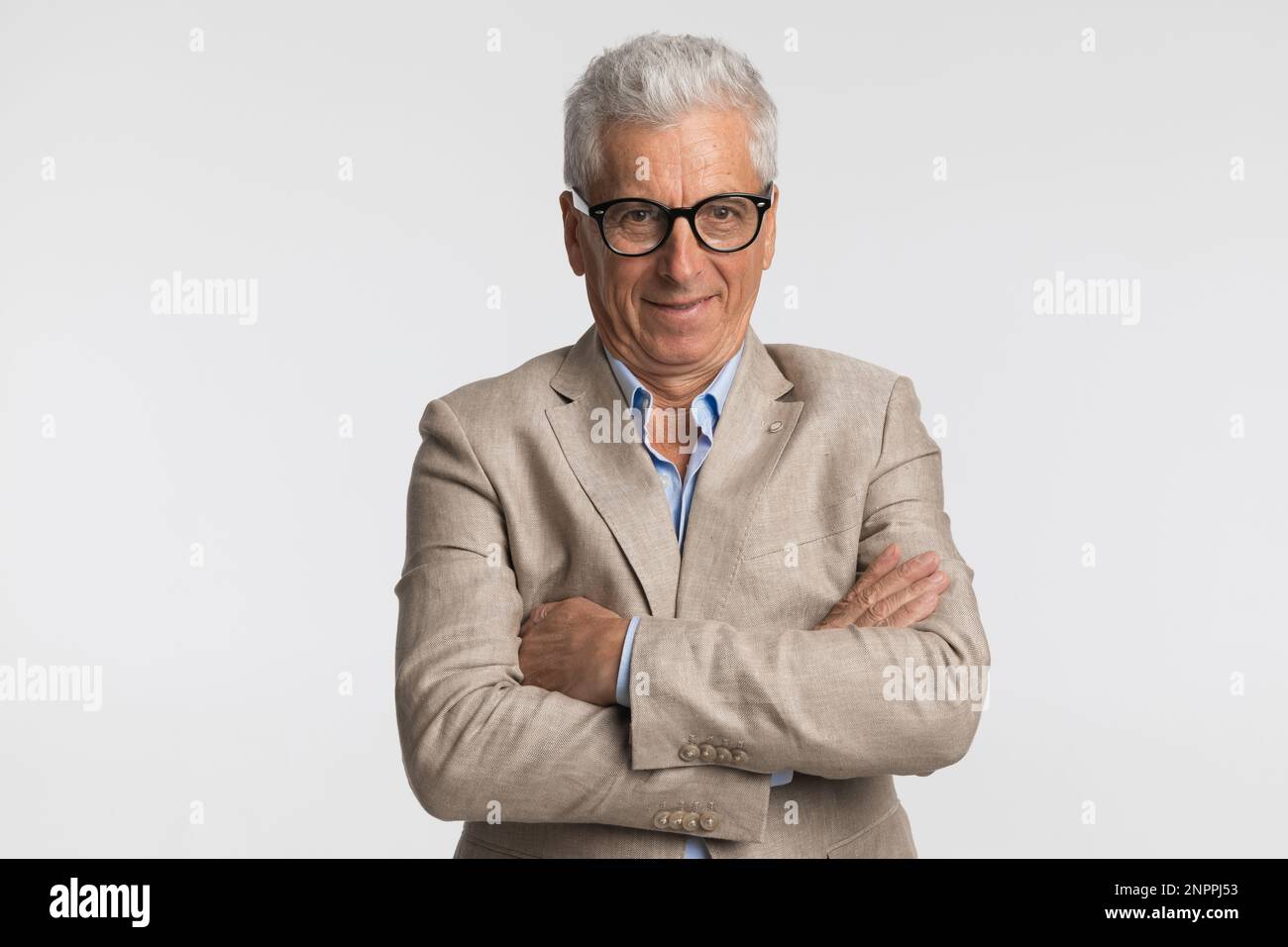 Eleganter alter Mann mit weißen Haaren in seinen 60s Jahren, Anzug und faltbaren Armen, lächelnd und selbstbewusst auf grauem Hintergrund Stockfoto