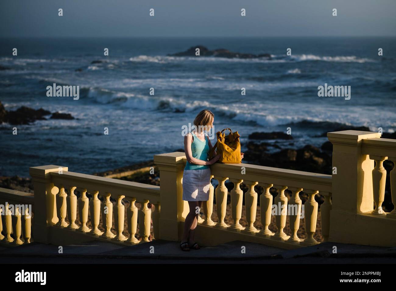 Eine Frau mit einem gelben Rucksack steht an der Atlantikküste in Porto, Portugal. Stockfoto