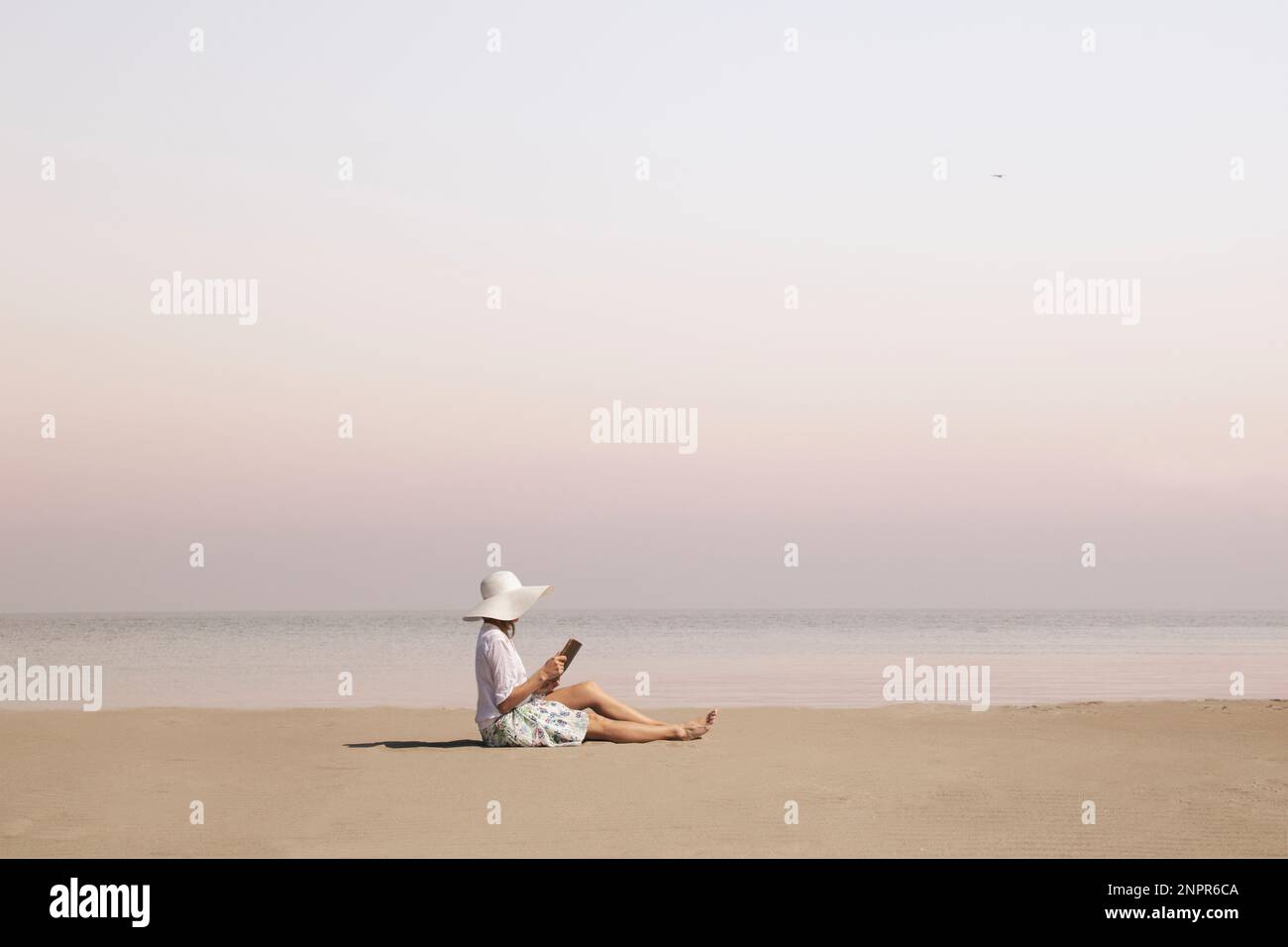 Eine Frau mit Hut liest ein Buch am Strand Stockfoto