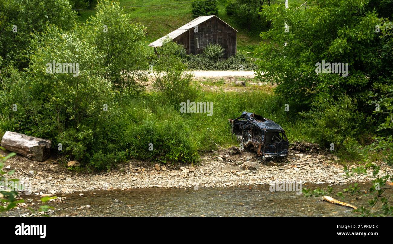 Verlassenes, zerstörtes Auto am Flussufer. Stockfoto