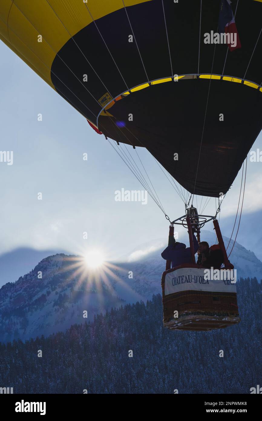 Ein Ballon, der mit Sonnenschein über eine Bergkette der schweizer alpen fliegt. Aufgenommen beim 42. International Balloon Festival in Chateau D'Oex im Januar Stockfoto