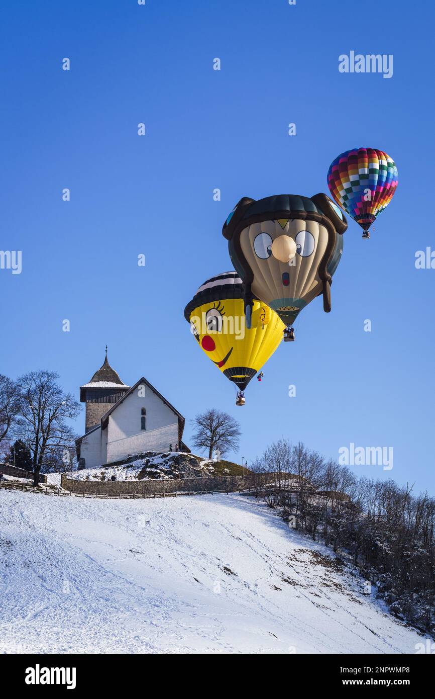 Drei Ballons über dem Kloster im Chateau D'Oex. Aufgenommen beim 42. Internationalen Ballonfestival in Chateau D'Oex im Januar 2023. Stockfoto