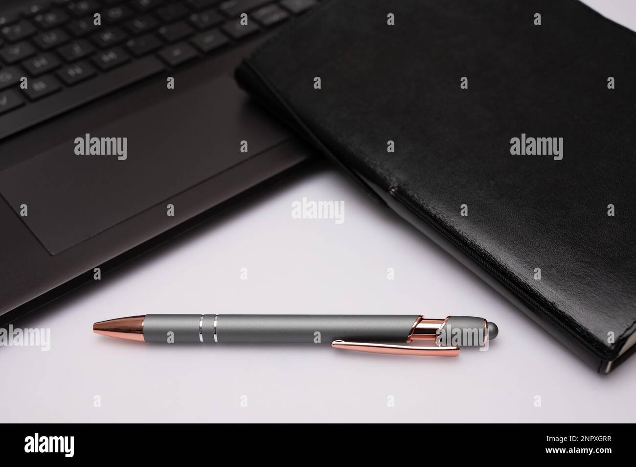 Ein schwarzes Notizbuch mit einem Stift und einem Computer auf einem Desktop, das ein Gefühl für ein Heimbüro oder kreatives Schreiben vermittelt. Stockfoto