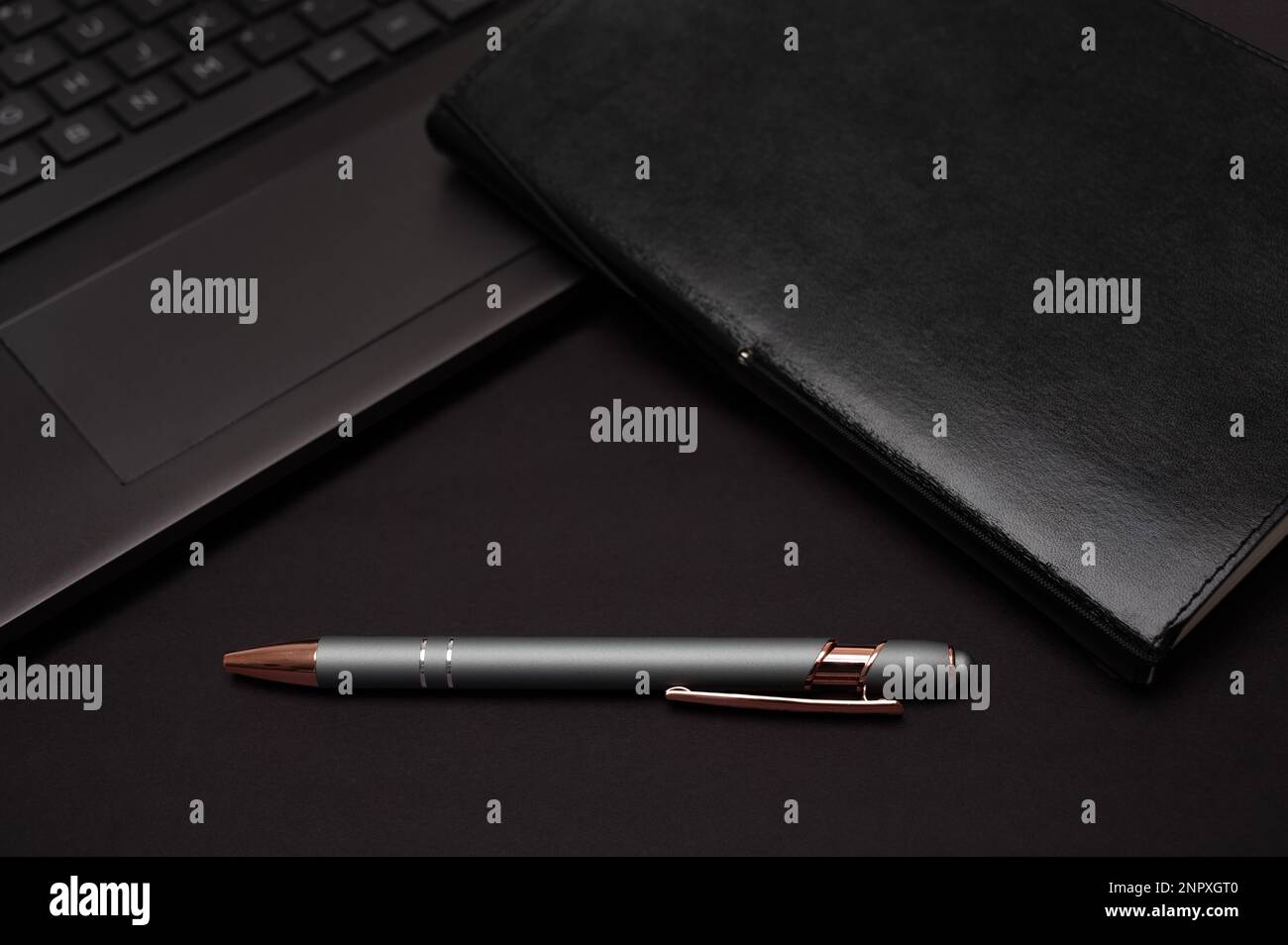 Ein organisiertes schwarzes Notebook, Laptop und Stift mit dem Gefühl eines Heimbüros oder kreativen Schreibens auf schwarzem Hintergrund. Stockfoto