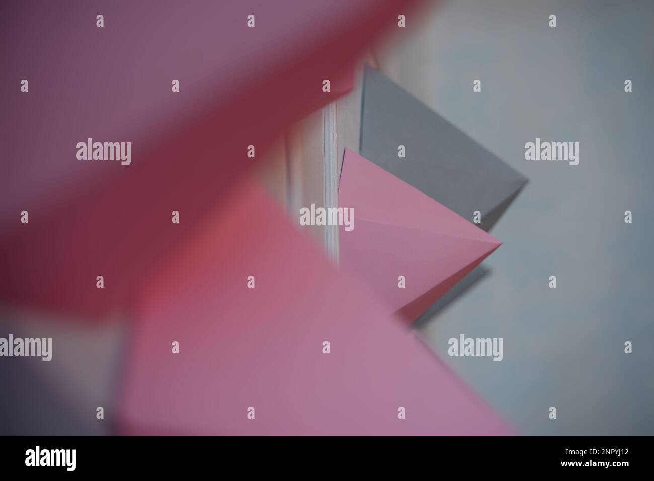 Abstrakter Hintergrund von Papierpolygonen in Grau, Pink, verschiedenen Formen auf einer weißen Wand. Kreative Inneneinrichtung. Dynamische Figuren im Innenraum. Origami h Stockfoto