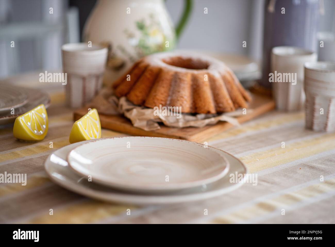 Osterzitronenkuchen, Babka mit Puderzucker auf einem festlichen Tisch, dekoriert mit Keramikschüsseln. Rustikaler, skandinavischer Stil mit Tischset Stockfoto