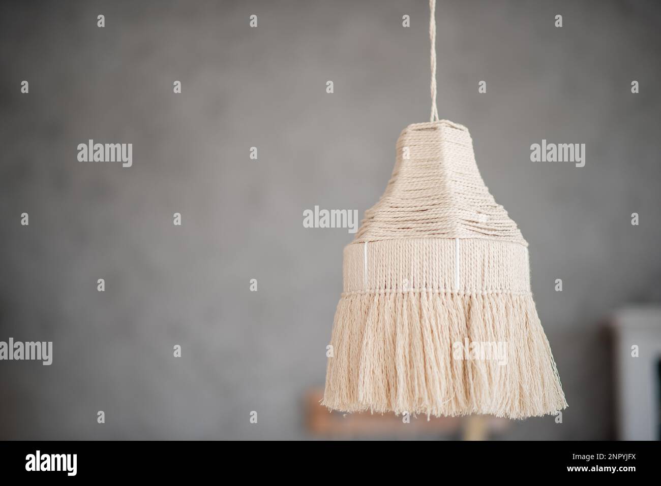 Die Makrame-Lampe hängt auf einem grauen, einfarbigen Hintergrund. Handgemachtes Hobby. Dekoration im Boho-Stil. Skandinavische Wohnungseinrichtung. Trendige Designdetails. Beige Stockfoto