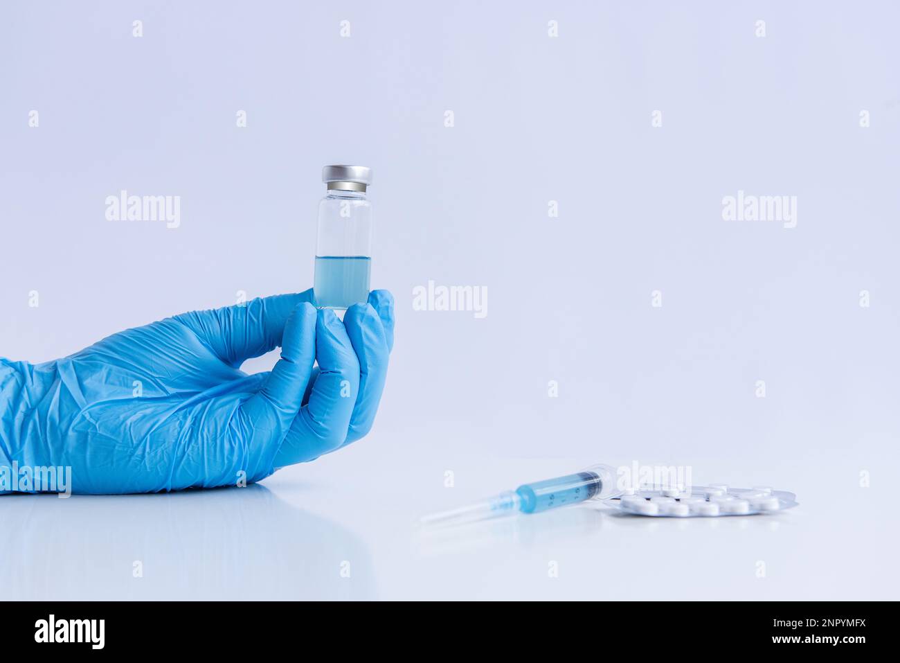 Auf weißem isoliertem Hintergrund halten die Hände des Arztes in medizinischen blauen Handschuhen eine Ampulle Impfstoff gegen Virus Coronovirus. Spritze mit Gegenmittel, Schmerztabletten Stockfoto