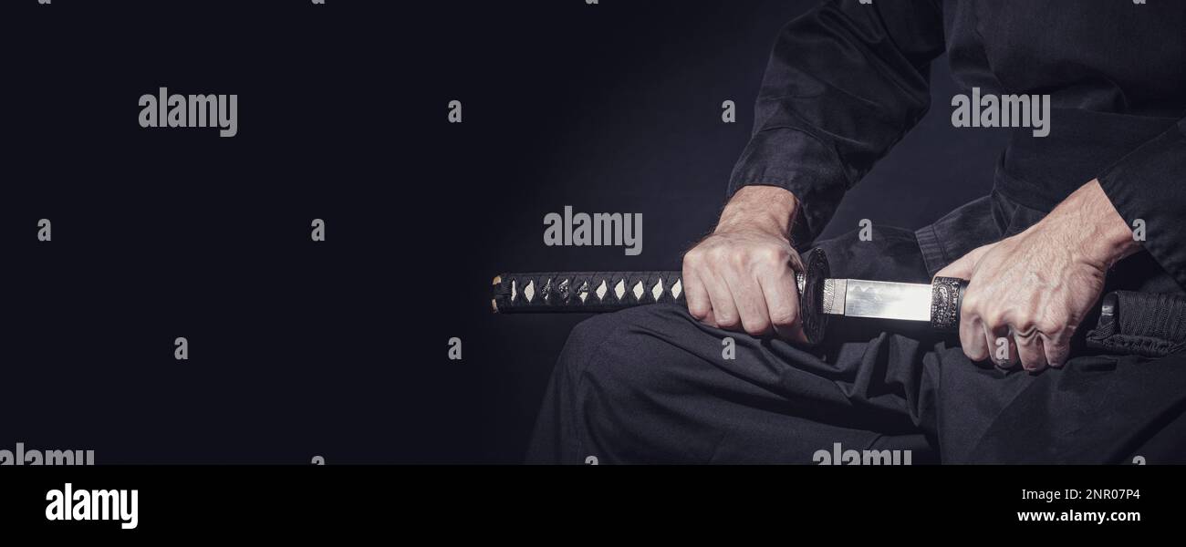 Der Samurai hält ein japanisches Katana-Schwert, Banner. Foto eines Kriegers in schwarzer Kleidung in niedriger Tonart mit Platz für Text Stockfoto