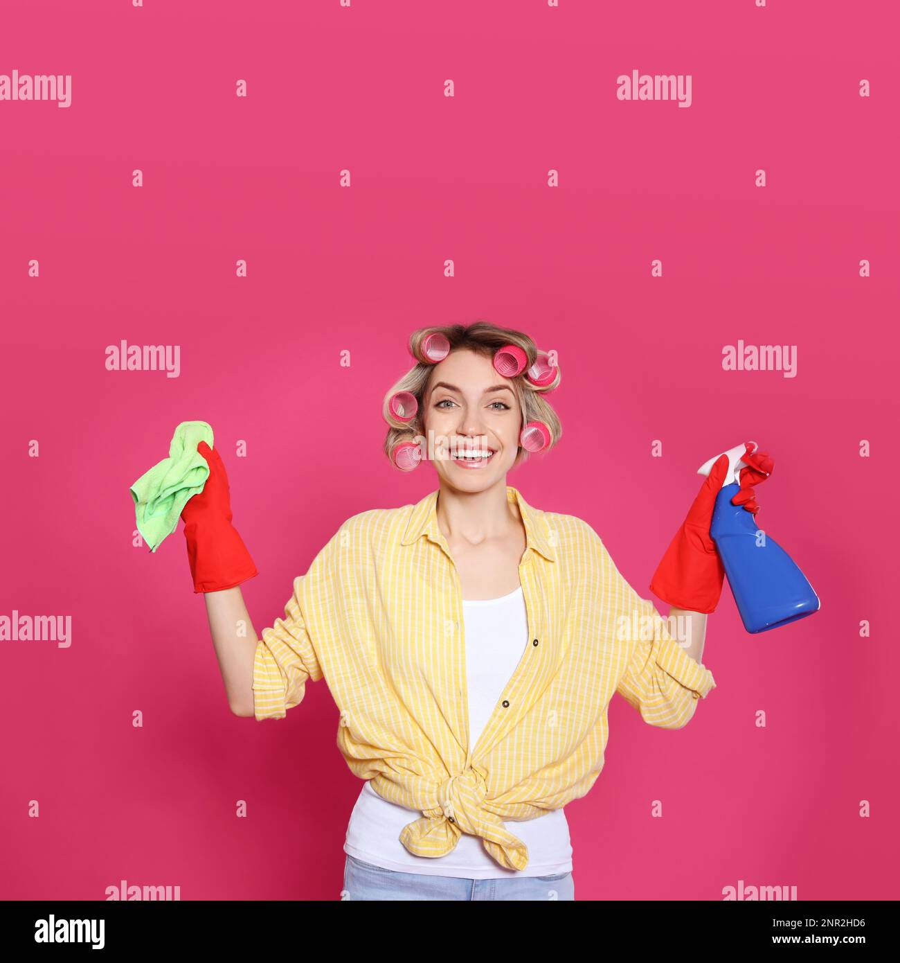 Junge Hausfrau mit Reinigungsmittel und Lappen auf rosa Hintergrund Stockfoto