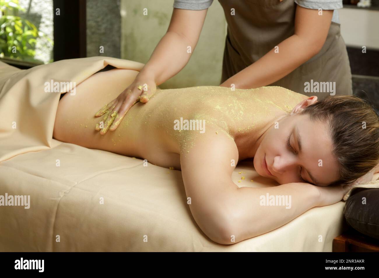 Junge Frau im natürlichen Schönheitsbad, die Körperpeeling-Behandlung bekommt. Relaxation, Entgiftung, Exfoliation des Hautrejuvenationskonzepts. Stockfoto